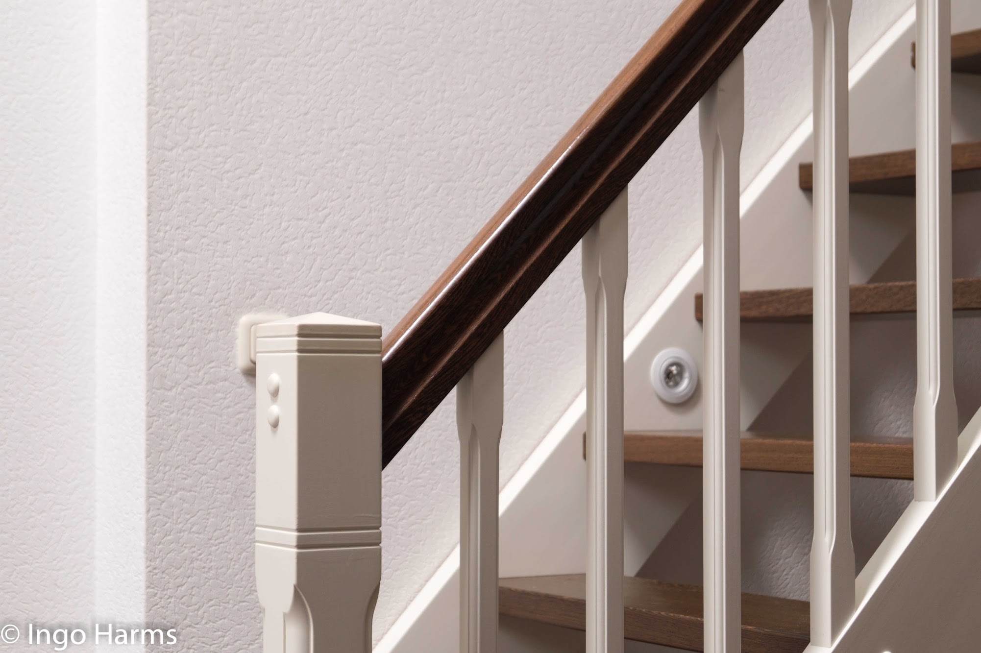 Detail eines weißen Treppengeländers mit dunklem Holzhandlauf